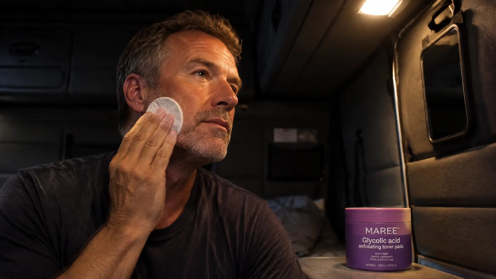 Hand swiping a MAREE glycolic acid toner pad across a cheek in a dim truck sleeper cab