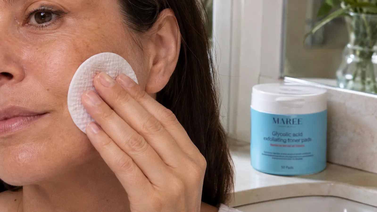 Hand holding a MAREE glycolic acid pad against a clean, dry cheek