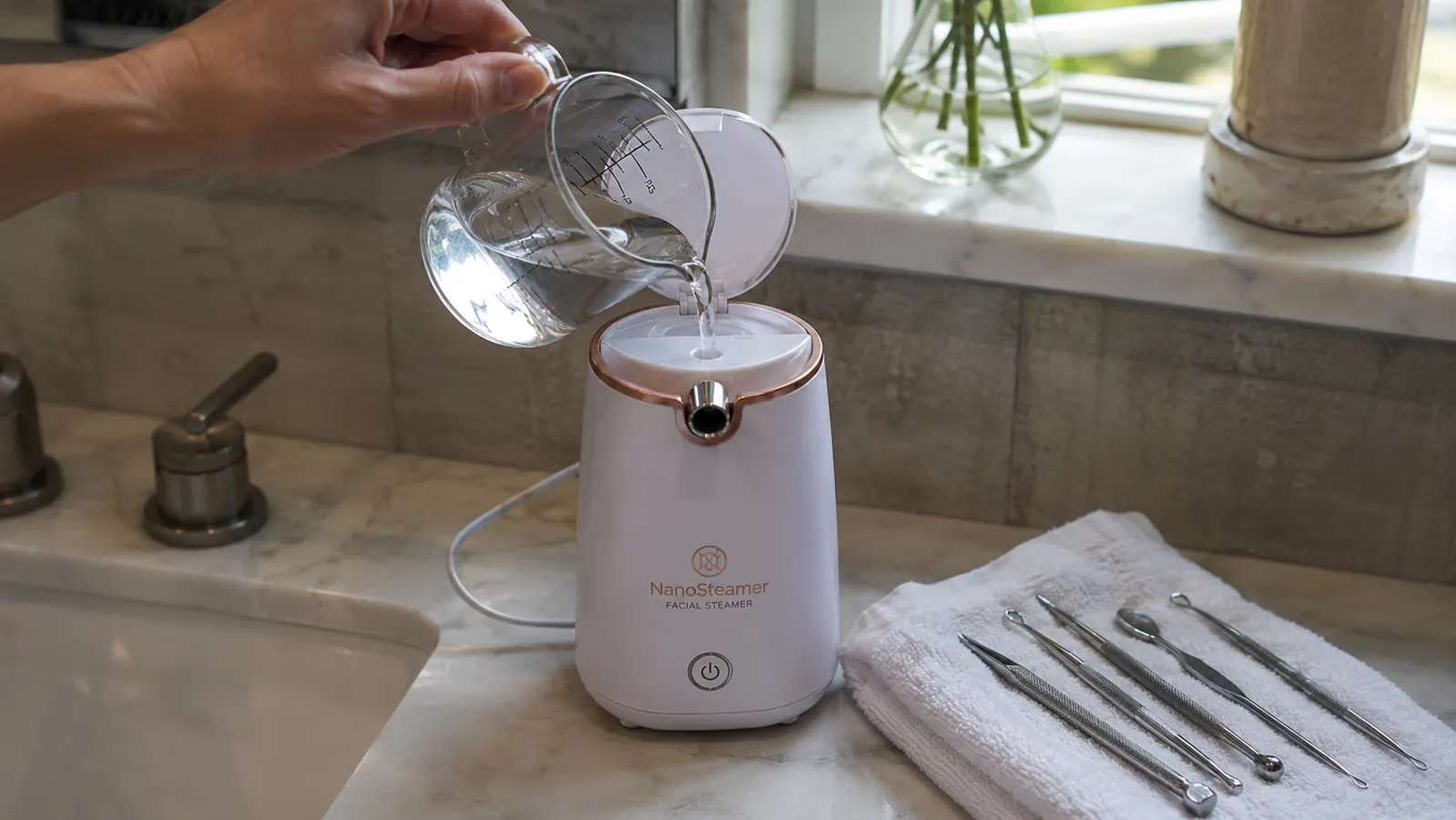 Close-up of a hand filling the NanoSteamer's water tank at a bathroom sink before a steaming session