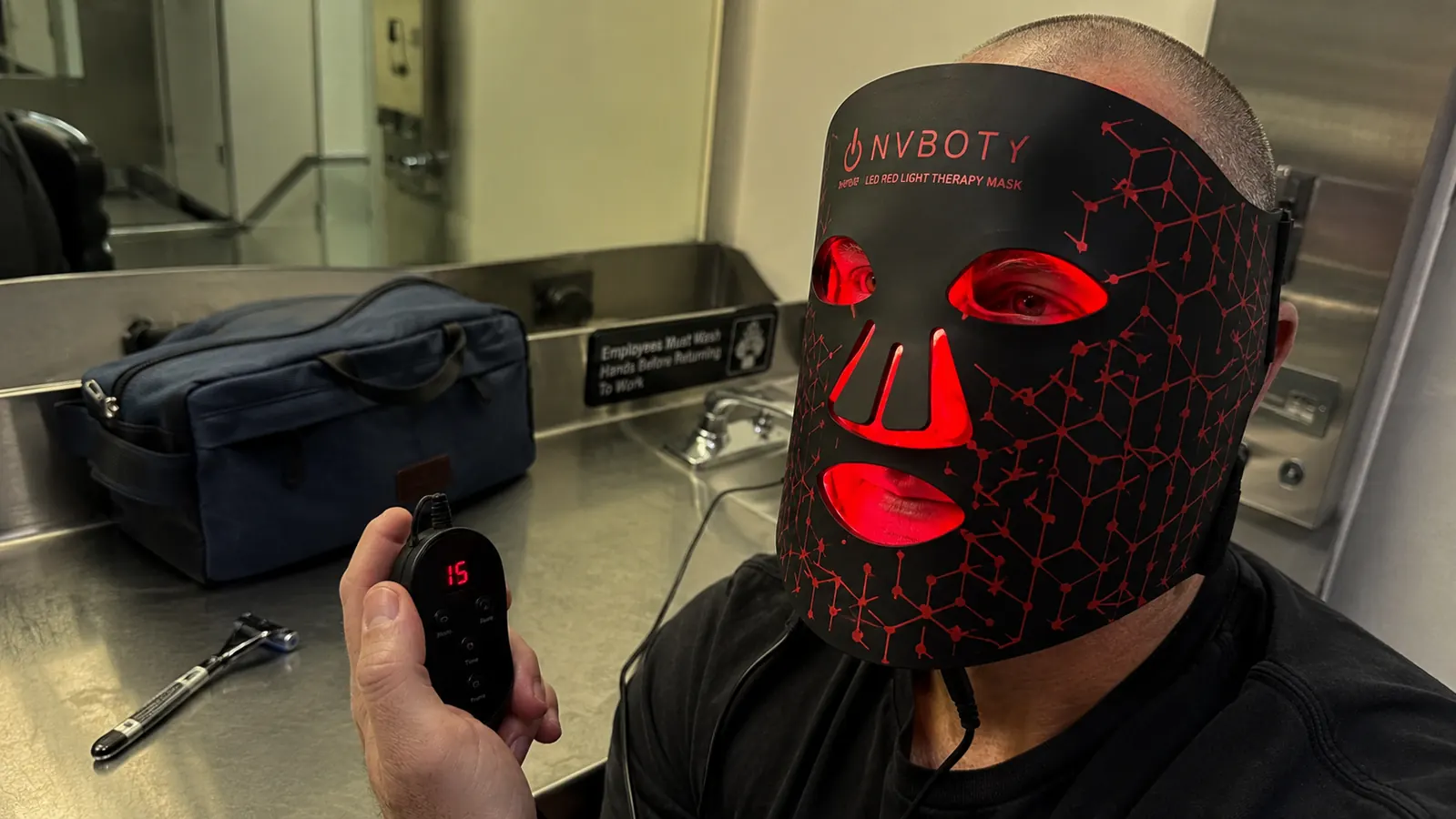 Close-up of the NVBOTY mask and its remote sitting on a truck stop bathroom counter next to a shaving kit
